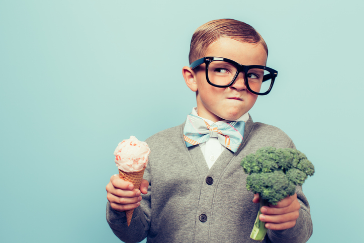 Young boy holding an ice cream cone in one hand and broccoli in the other.