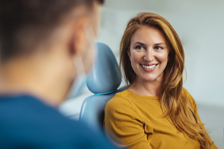 Smiling red-haired woman listening to her prosthodontist while sitting in his office