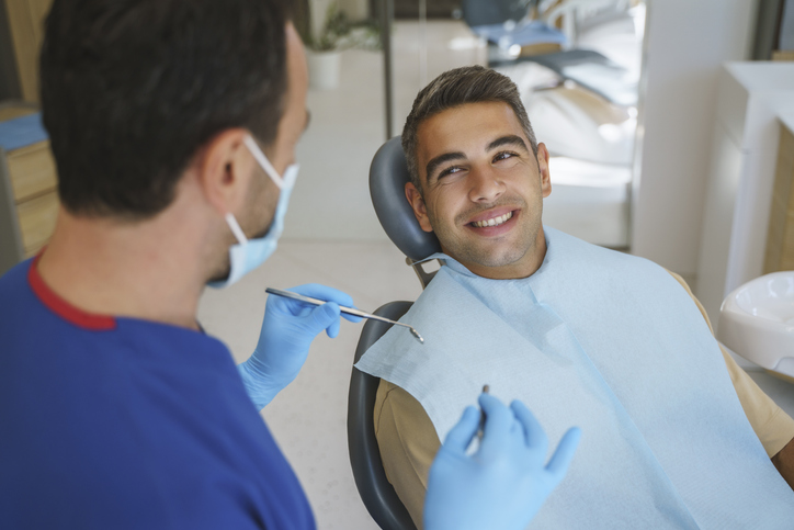 male dental patient smiling and sitting in dental chair, dentist with dental tools