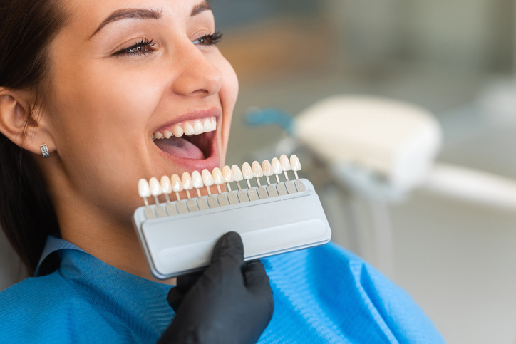 A beautiful young female patient uses a dental tooth shade guide for whitening teeth service to ensure a perfect choice of color.