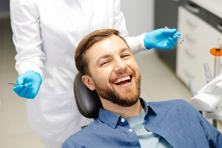 happy man sitting at dentist chair in modern clinic enjoying dental treatment with professional dentist